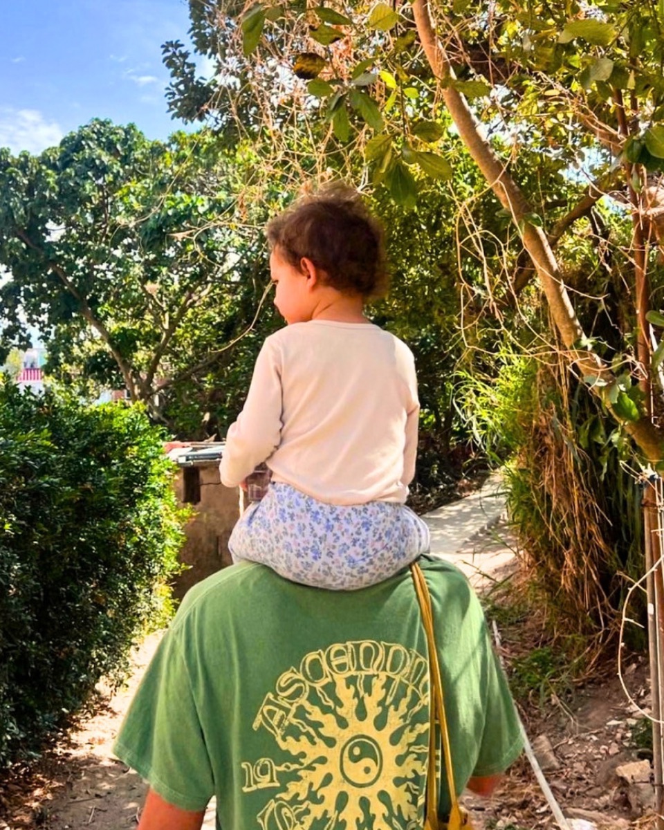 Dani Sierra walking a garden path, daughter riding on shoulders
